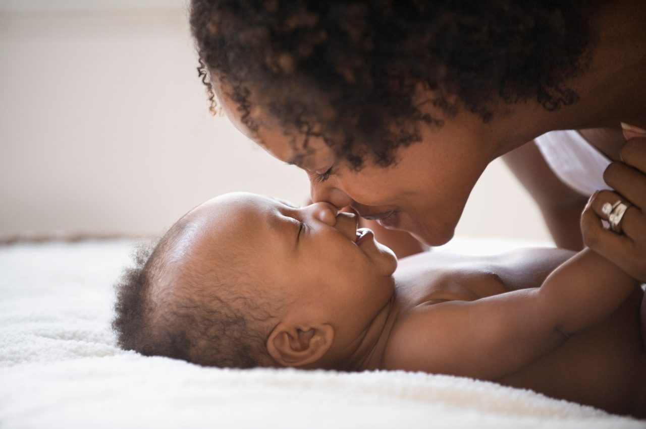 Mom plays with baby on the bed by giving baby lots of kisses