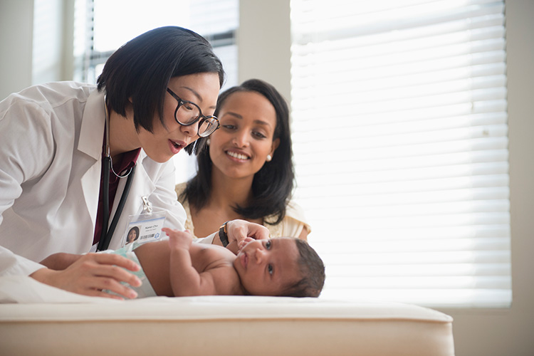 Happy pediatrician examines a newborn baby while mom looks on
