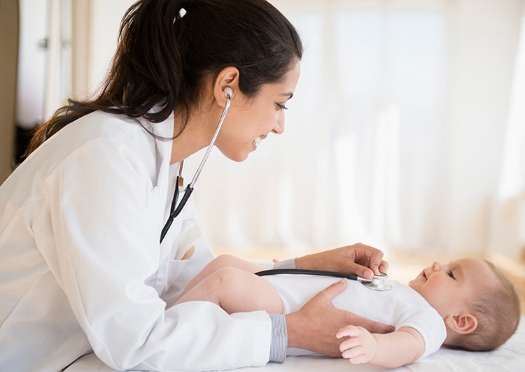 Smiling doctor taking the heartbeat of a happy baby with a stethoscope