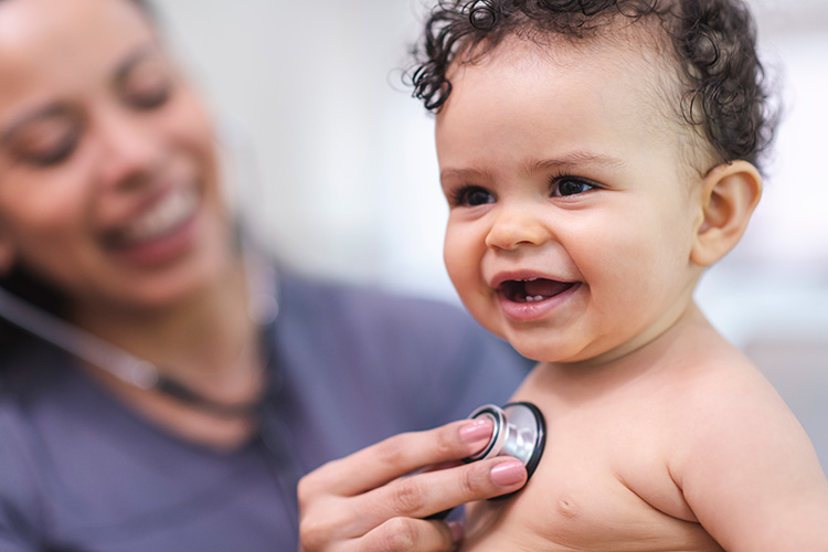 A smiling doctor listens to a smiling baby's heartbeat with a stethoscope