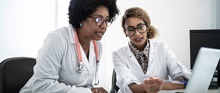 Two doctors discuss research they are viewing on a computer screen