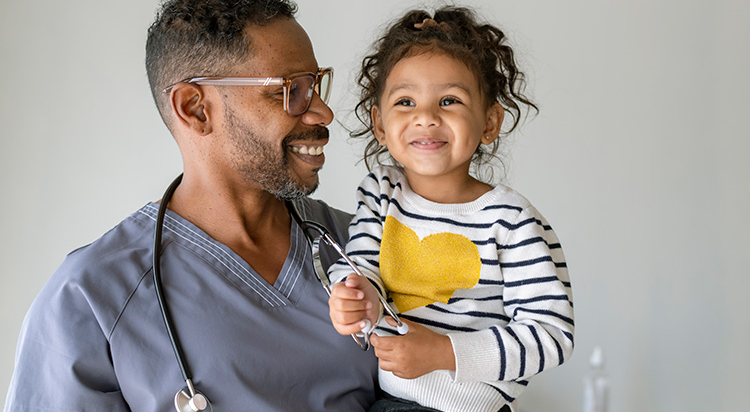 A smiling doctor holds up a happy toddler 