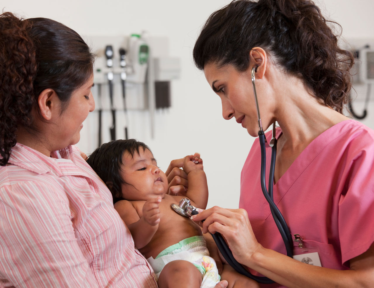 Happy pediatrician examines a newborn baby while mom looks on