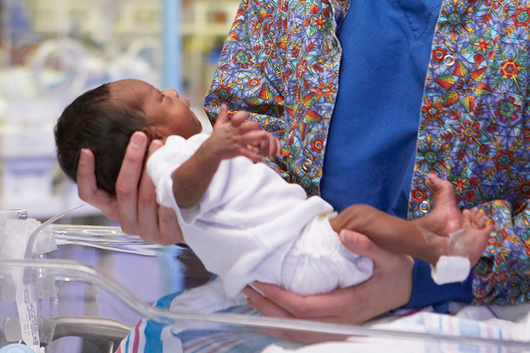 Healthcare Provider picks up a newborn baby a hospital bassinet