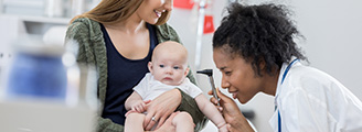 A mother holds her baby so that a pediatrician can examine the baby's ear with an otoscope