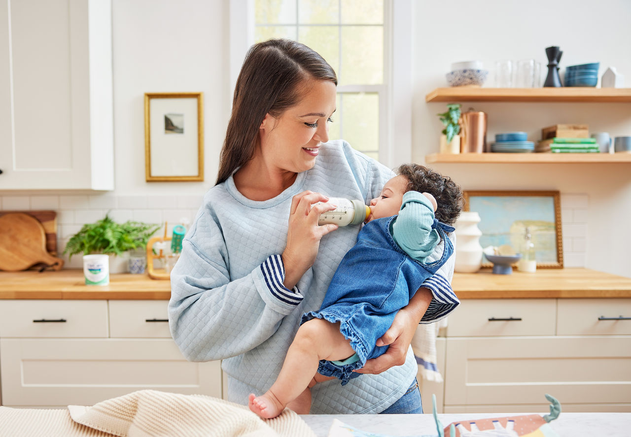 Smiling mother bottle feeding baby in the kitchen