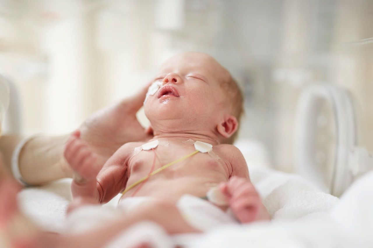 Premature baby being held through incubator