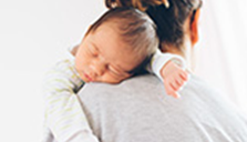 A baby takes a nap on a parent's shoulder