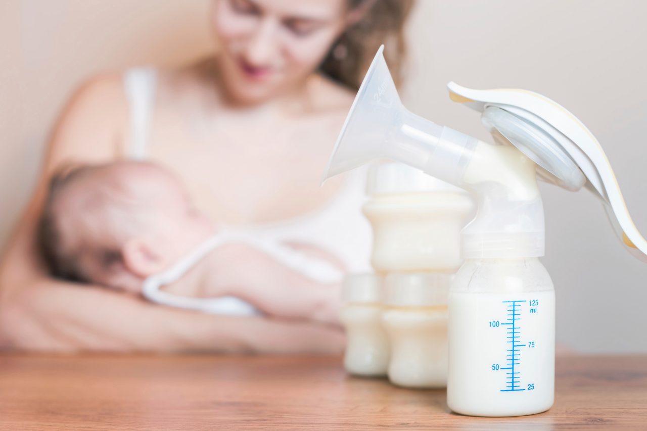 Mother holding baby with pumped breastmilk in the foreground