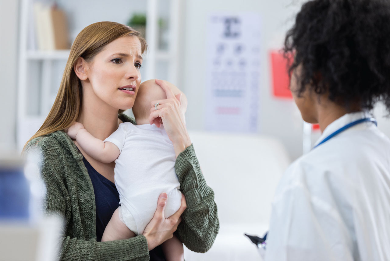 Mother with postpartum depression holding her baby and discussing with doctor