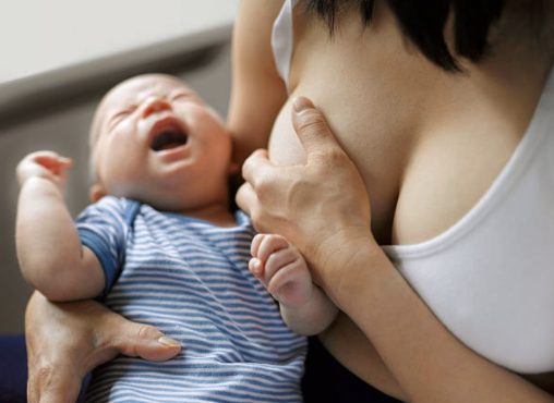 Mother holding breast in discomfort while baby is crying