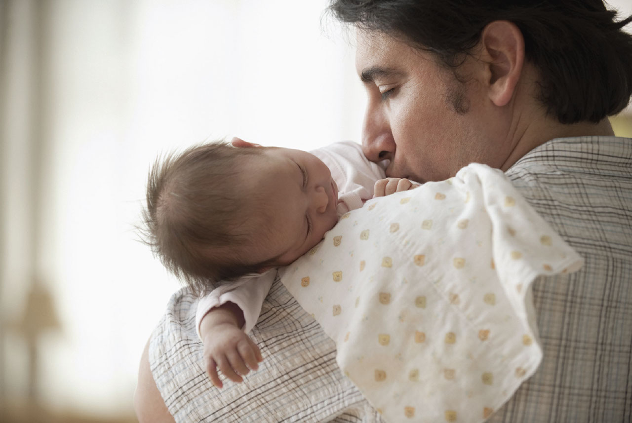 Dad holding a sleeping newborn baby and giving baby a kiss