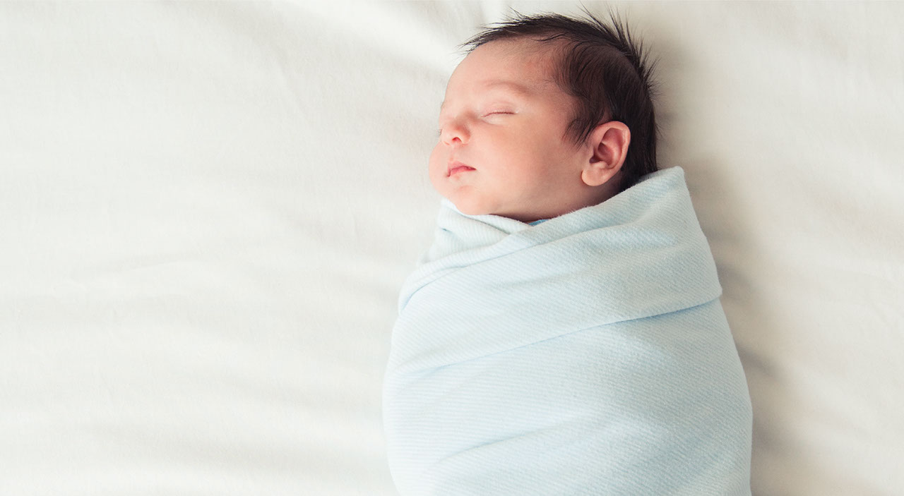 Full term baby boy wrapped in blue swaddle sleeping