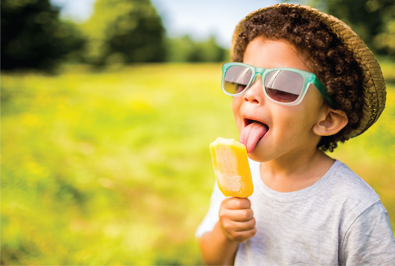Healthy young boy licking a popsicle outside on a warm sunny day